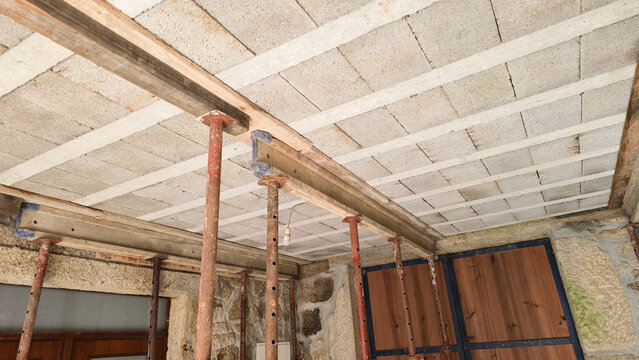 Adjustable steel props support a ceiling during structural home renovation. Concepts: construction safety, temporary support, building repair, structural reinforcement.