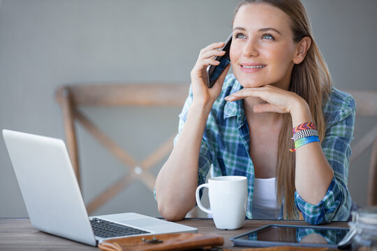 Young Woman Working on Laptop and Talking on Phone