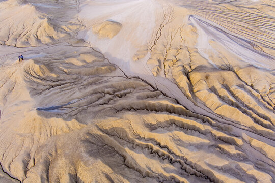 Aerial view of the Mud Volcanoes of Paclele Mari, showing the unique, cratered, and cracked landscape with grey mud flows and two people standing on the terrain in Paclele, Buzau County, Romania.
