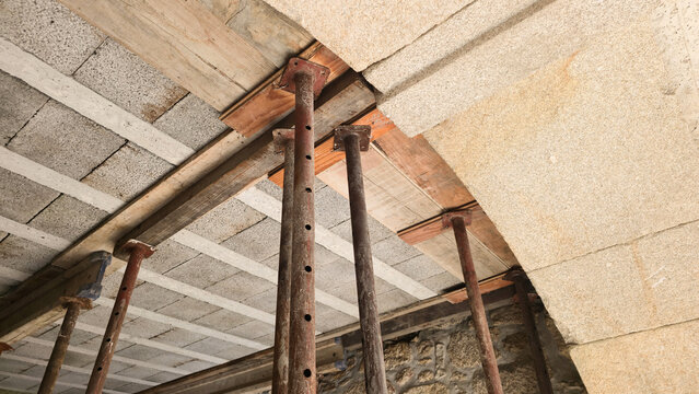 Adjustable steel props support a ceiling during structural home renovation. Concepts: construction safety, temporary support, building repair, structural reinforcement.