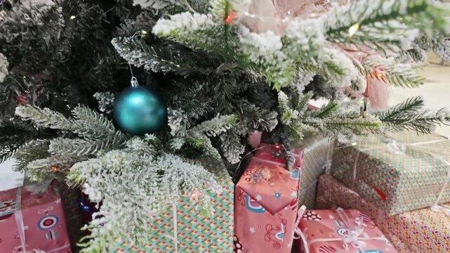 Snow-covered Christmas tree branches with a blue ball above colorful wrapped gift boxes.