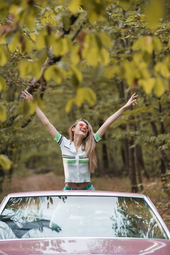 Joyful road trip adventure of happy woman in a pink vintage convertible through autumn foliage