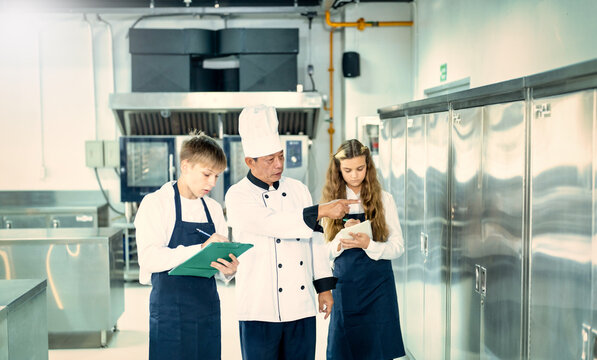 Senior male chef teaches young teenage boys cooking in school kitchen. Education Concept