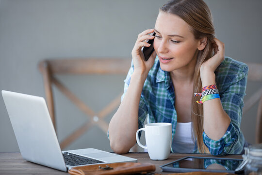 Young Woman Working on Laptop and Talking on Phone