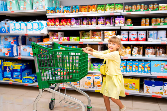 Young girl pushing a shopping cart in supermarket aisle, doing groceries with family