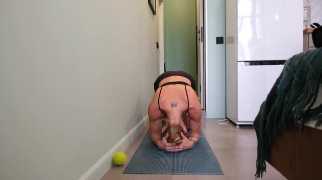 Mourning routines. middle adult woman training yoga headstand at small apartment in narrow corridor on training mat
