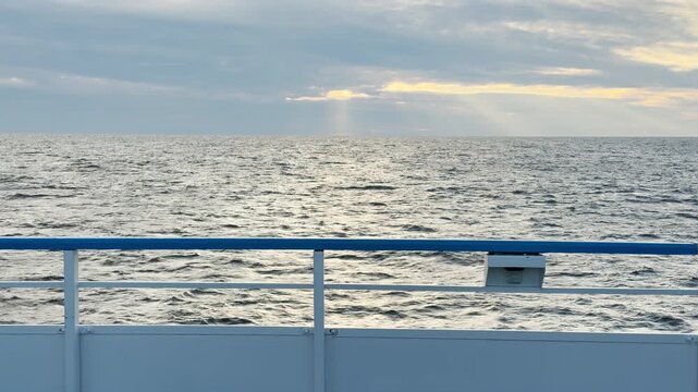 A cruise ship railing looks out across the rippling waters of Lake Ladoga under a cloudy sky. Sunbeams shine through. This serene view brings a feeling of peace and quiet relaxation.