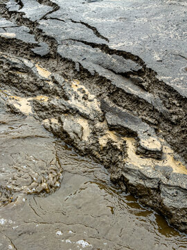Aerial view of cracked and eroded asphalt road surface with muddy water runoff and soil deposits in Latvia.