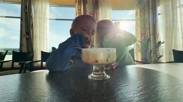 A happy boy enjoys dessert at a table on a cruise ship. Bright sunlight fills the room as they sail across Lake Ladoga. This sweet moment creates a joyful feeling of family warmth.