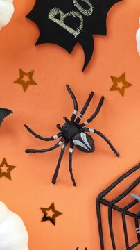 Top view of plastic spider and black bats spinning on orange background in vertical orientation, Halloween holiday decoration rotating. Spooky seamless background. Halloween backdrop
