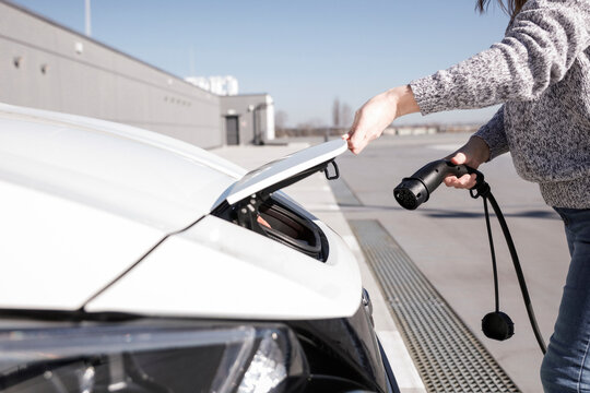 Data Set Training &ndash; woman charging electric car with EV charging station. Parking area background, providing a realistic everyday environment for electric vehicle charging.