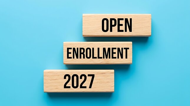 Open enrollment 2027 plan is written on three wooden blocks stacked like stairs on blue background as concept for annual healthcare policy registration planning.