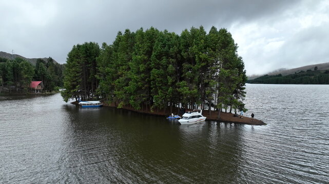Aerial view of Corani Lake with boats docked at a small island covered in dense pine trees under a cloudy sky in Chapare, Cochabamba Department, Bolivia.
