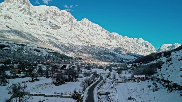 Albania, Boge 11 01 2026: Still 4K drone video of snow-covered Boge showing houses, a car driving along the road, frozen Prroni i Thate riverbed, and sunlit Albanian Alps.