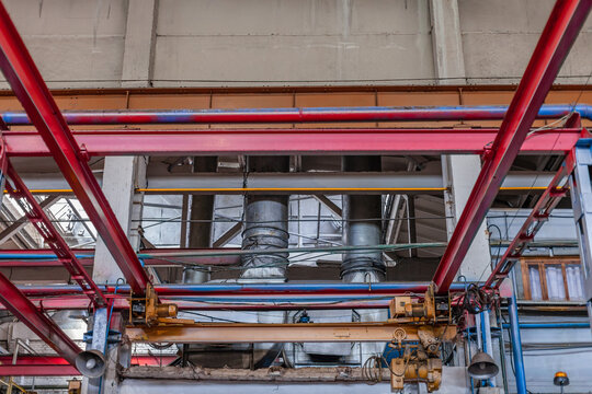 Industrial infrastructure with red metal beams, ventilation pipes, overhead crane system inside large factory. Industrial interior, mechanical engineering, heavy machinery, construction environment.