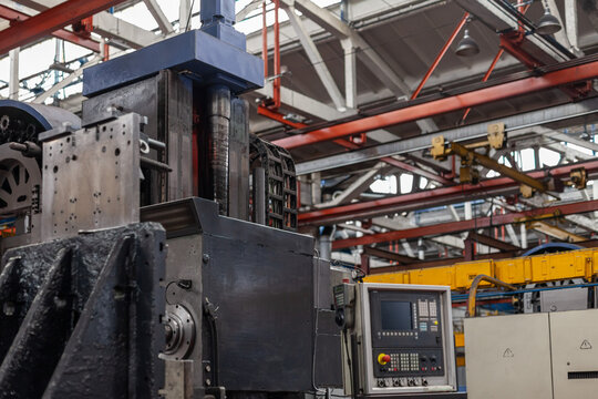  Intricate metal structure of equipment with control console. Industrial heavy machinery within large-scale manufacturing plant. Mechanical precision, factory environment.