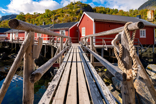 Rustic wooden walkway leads to traditional red rorbuer on stilts in the historic fishing village of Nusfjord in the Lofoten Islands.