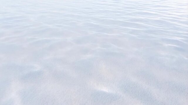 Calm water surface with gentle ripples flows smoothly under soft light reflections in pale blue and white tones. Flowing motion creates soft reflections and visible depth.