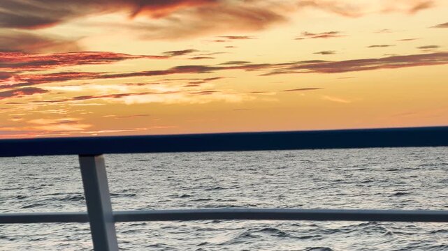 A cruise ship railing frames vibrant sunset clouds over Lake Ladoga. Fiery red and golden light fills the sky, bringing a peaceful and romantic mood. The view inspires awe and calm.