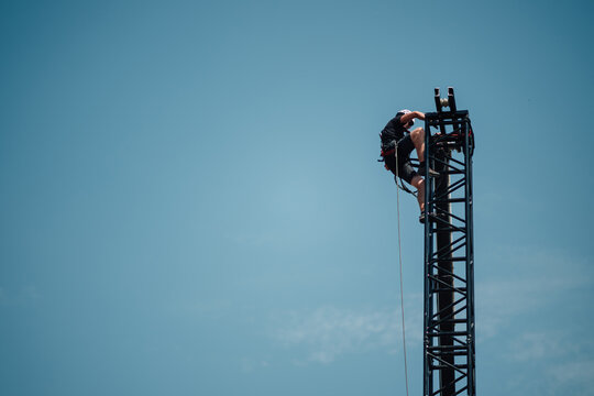 Professional rigger climbing and adjusting equipment on a tall steel truss structure, ensuring safety with harness and rope