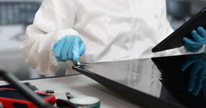 Technician wearing blue gloves uses a tablet screen beside electronic repair tools in a clean workshop, device maintenance and digital diagnostics.