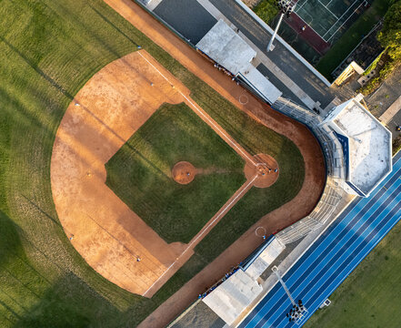 Aerial view of a baseball field with a dirt infield and green grass outfield, adjacent to a running track in Santo Domingo, Distrito Nacional, Dominican Republic.