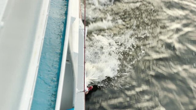 A mop is rinsed overboard from a cruise ship into the river water. The dynamic motion creates splashing foam. This unusual sight brings a feeling of curious amusement.
