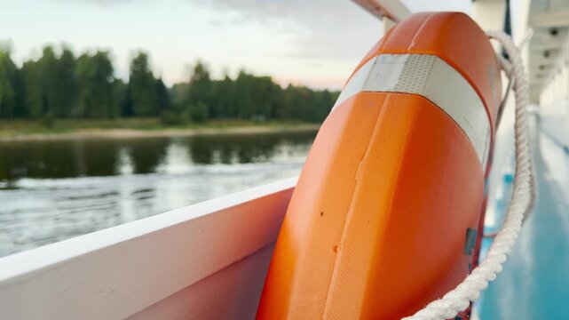 A bright orange lifebuoy rests on the cruise ship railing overlooking the river. A safe, calm, and secure feeling inspires peace during this serene journey.