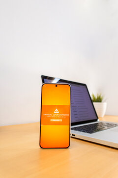 Smartphone displaying unusual login detected alert with laptop in background