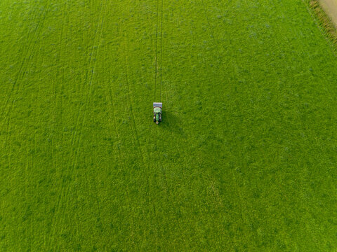 Aerial view of a green tractor working in a large vibrant green field with visible tire tracks in Looe, Cornwall, United Kingdom.