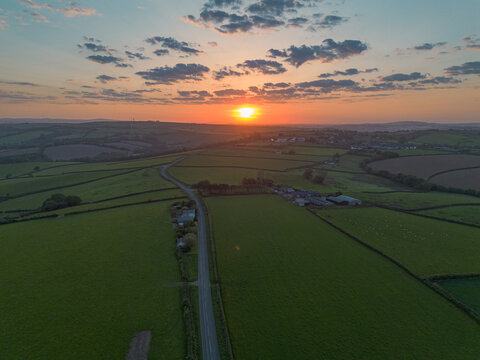 Aerial view of rolling green fields and a winding road at sunset in the countryside Looe, Cornwall, United Kingdom.