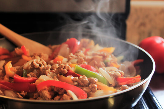Colourful peppers, onions and minced meat sizzling in a frying pan with rising steam during home cooking.