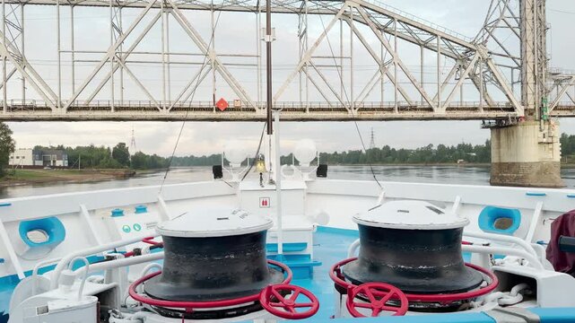 A cruise ship approaches and passes under a large metal bridge spanning the river. The impressive architectural structure creates an exciting sense of adventurous journey and anticipation.
