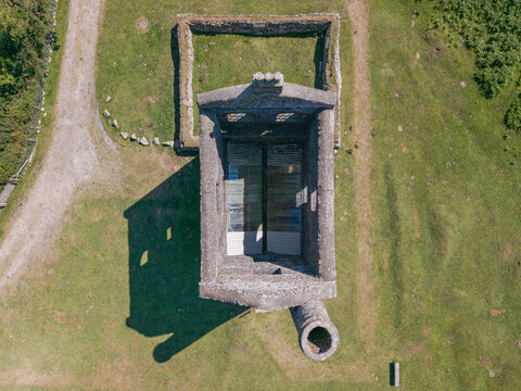 Aerial view of the historic stone mine engine house ruin surrounded by green grass and dirt paths in Minions, Cornwall, United Kingdom.