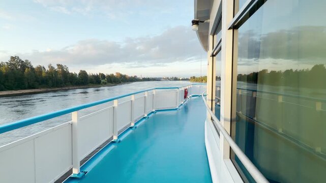 A cruise ship travels smoothly along a calm river. The blue deck offers a peaceful view of green shores under bright clouds. Travelers feel relaxed and joyful in this quiet moment.