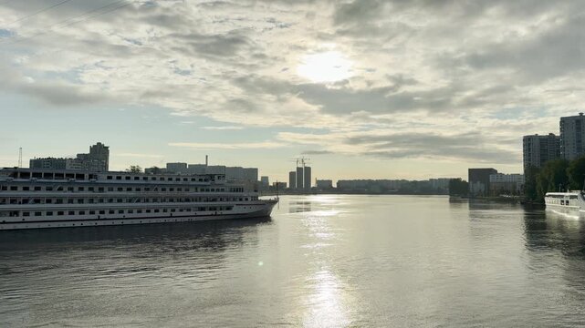 A cruise ship travels along the wide Neva River in Saint Petersburg. Sunbeams glisten on calm water beneath cloudy skies. This serene view inspires deep peace and tranquil joy.