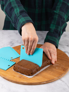 Teenager cutting cookie dough with blue plastic scraper on wooden tray, scraper set nearby, close-up of hands