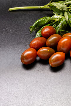 Brown plum-shaped tomatoes and basil on dark gray with copy space
