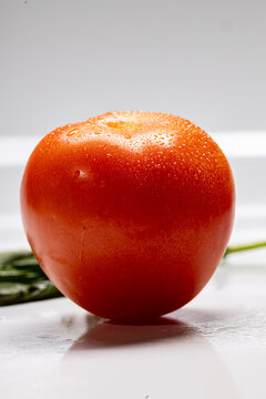 Single red tomato with water droplets on a light background