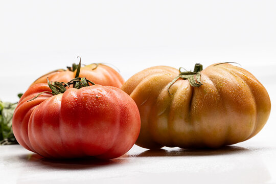 Three ribbed tomatoes in different colors on a light background