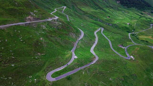 Aerial drone footage of hairpin switchbacks on the eastern side of Furka Pass, Switzerland, with descending lateral flight and counter-panning camera over green alpine terrain