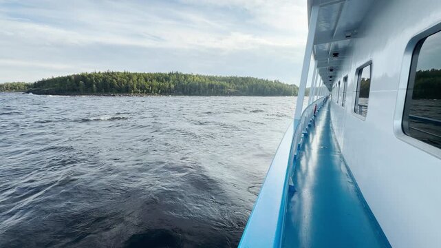 A cruise ship sails across Lake Ladoga toward Valaam. Choppy waters lap along green forested shores under a soft sky. Passengers feel peaceful joy and gentle excitement.