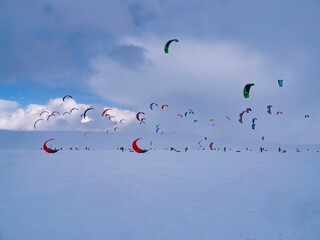 Berlevag, Norway - 24.03.2015: Colorful snowkites soaring over a vast white arctic tundra under a moody purple-blue overcast sky © Andrei