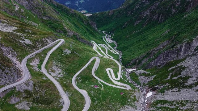 Aerial drone footage of the Tremola hairpin road descending into a mountain valley near the Gotthard Pass, Switzerland, with slow lateral flight and rotating camera