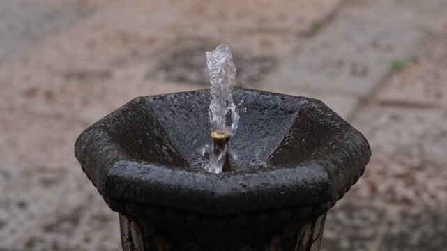 Water fountain releases a steady stream of water, highlighting the dynamic flow and surface texture against a rustic stone setting