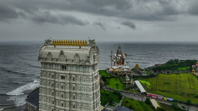 Aerial view of the towering Raja Gopura and the massive Shiva statue at Murudeshwar Temple overlooking the Arabian Sea under a cloudy sky in Murdeshwar, Karnataka, India.