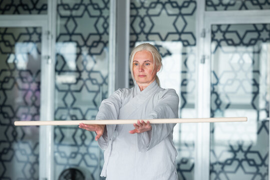 Senior woman practicing qigong with staff in studio