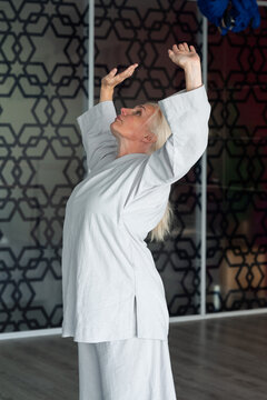 Senior woman practicing qigong indoors with raised arms
