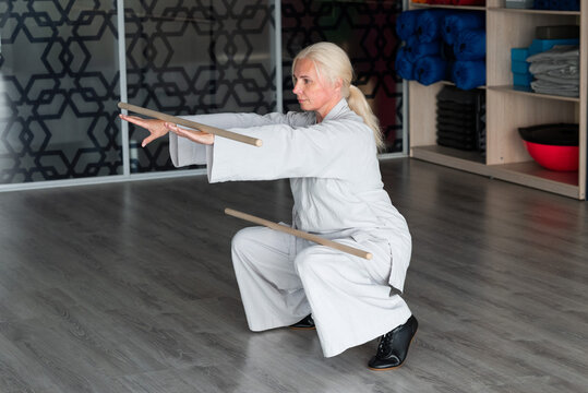 Senior woman practice qigong with wooden staff indoors