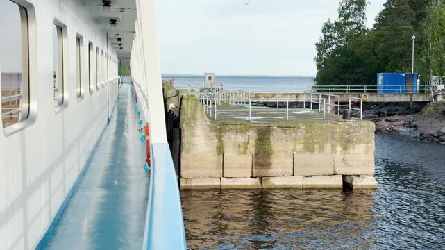 A cruise ship docks at a concrete pier on Lake Ladoga near Valaam. Green trees frame the quiet harbor. The gentle arrival brings peaceful joy and calm anticipation.